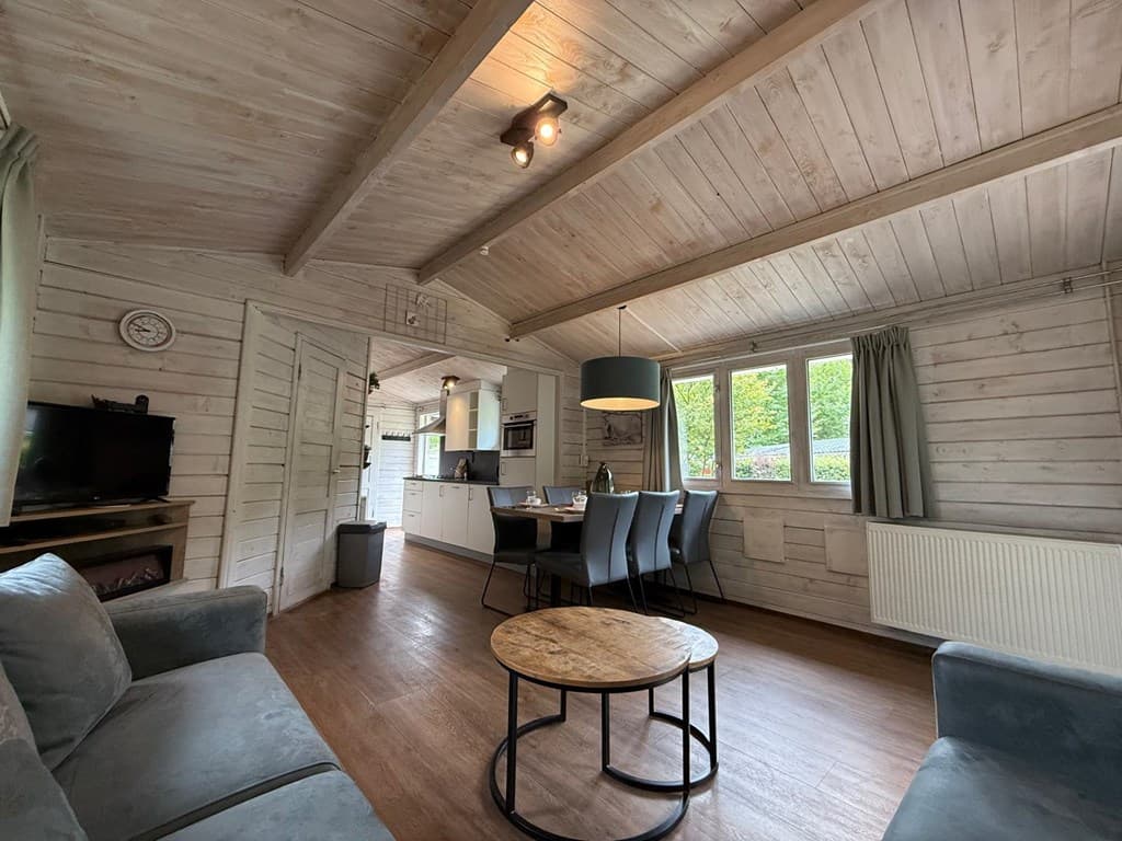 Moderne woonkamer met houten plafonds, eethoek en keukeninrichting, zachte kleuren en grote ramen voor natuurlijk licht