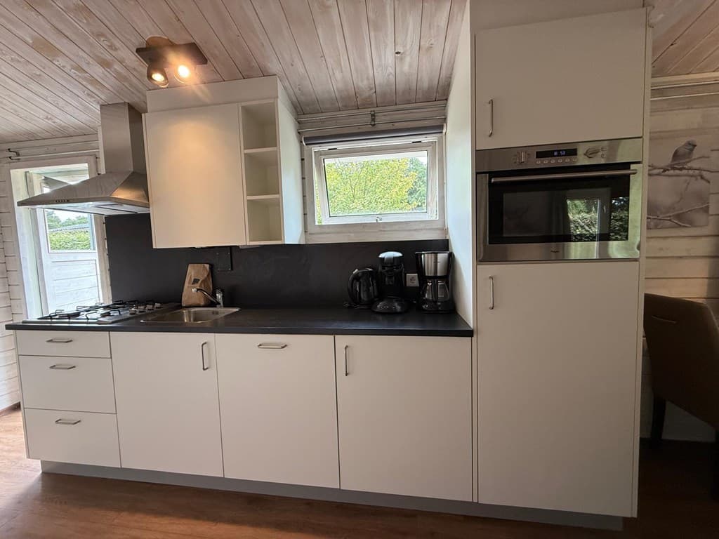 Hoekkeuken met moderne apparatuur, witte kasten en een houten plafond in een vakantiewoning.