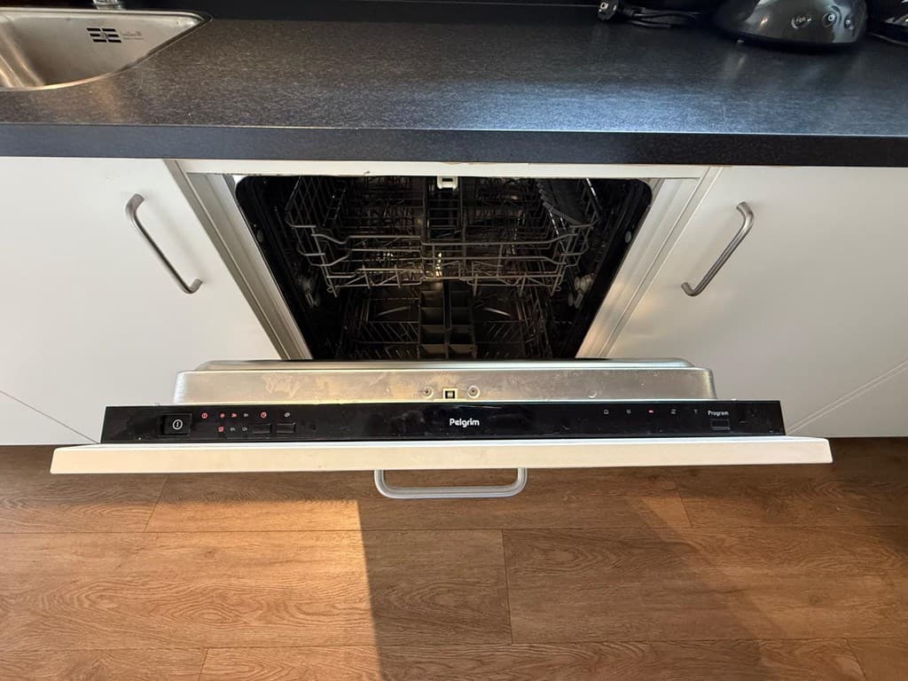 Open vaatwasser in een moderne keuken met een zwarte aanrecht en lichte kasten.