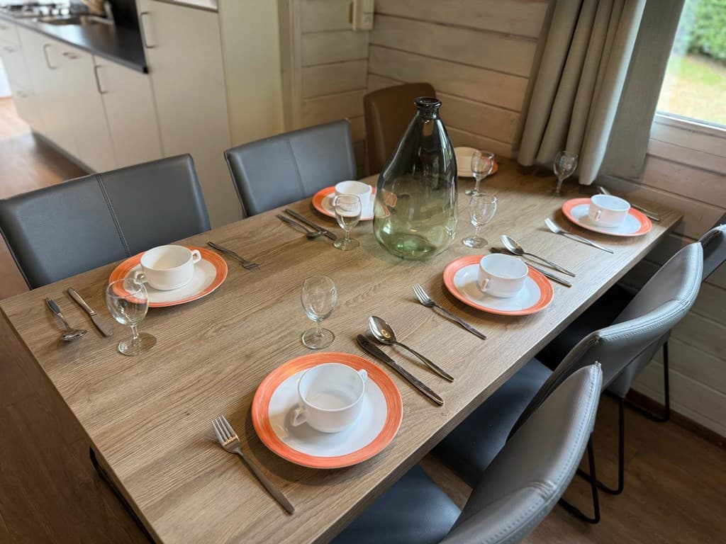 Eettafel met oranje borden en glazen, zichtbaar op een houten vloer met een keuken op de achtergrond.