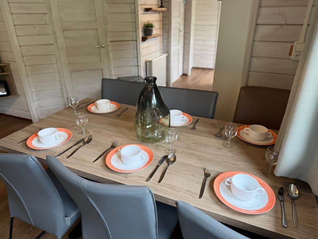 Eettafel met zes plaatsen, gedekt met servies en glazen in een moderne woonkamer met houten wanden.