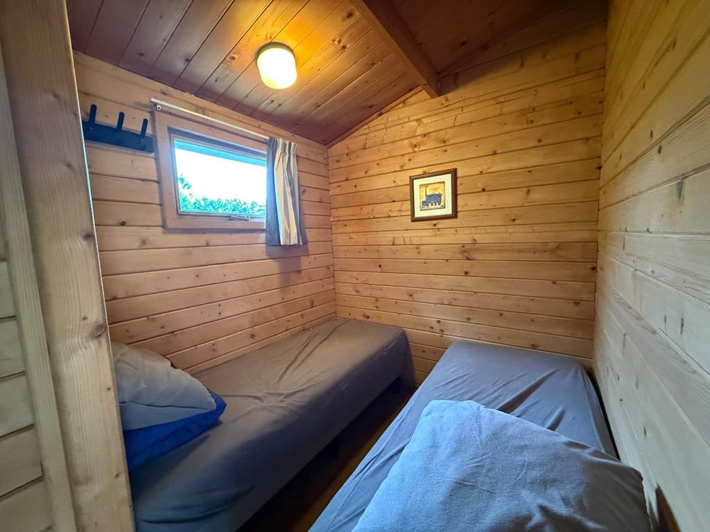 Binnenzicht van een houten slaapkamer met twee eenpersoonsbedden en een raam met gordijnen
