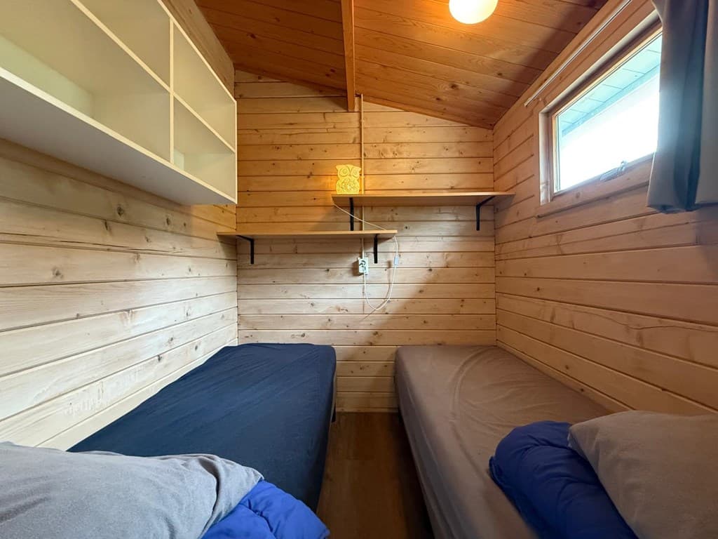 Slaapkamer met houten wanden, twee aparte bedden en een raam voor natuurlijk licht.