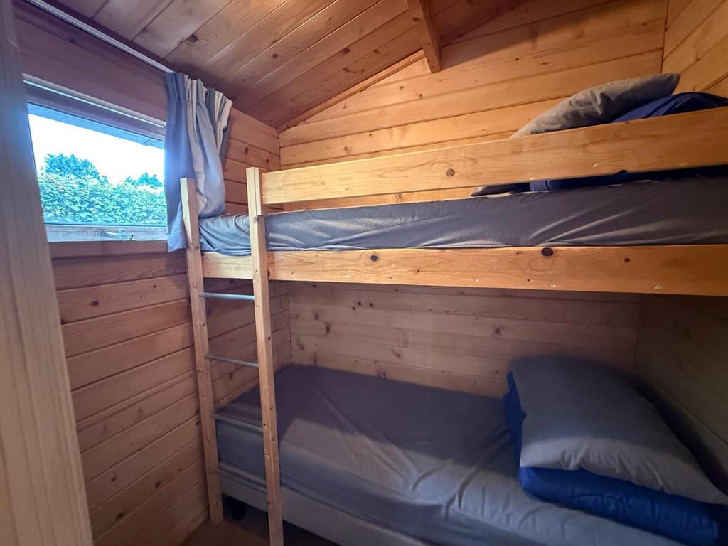 Houten slaapkamer met stapelbed en een eenpersoonsbed, raam met uitzicht op buiten.
