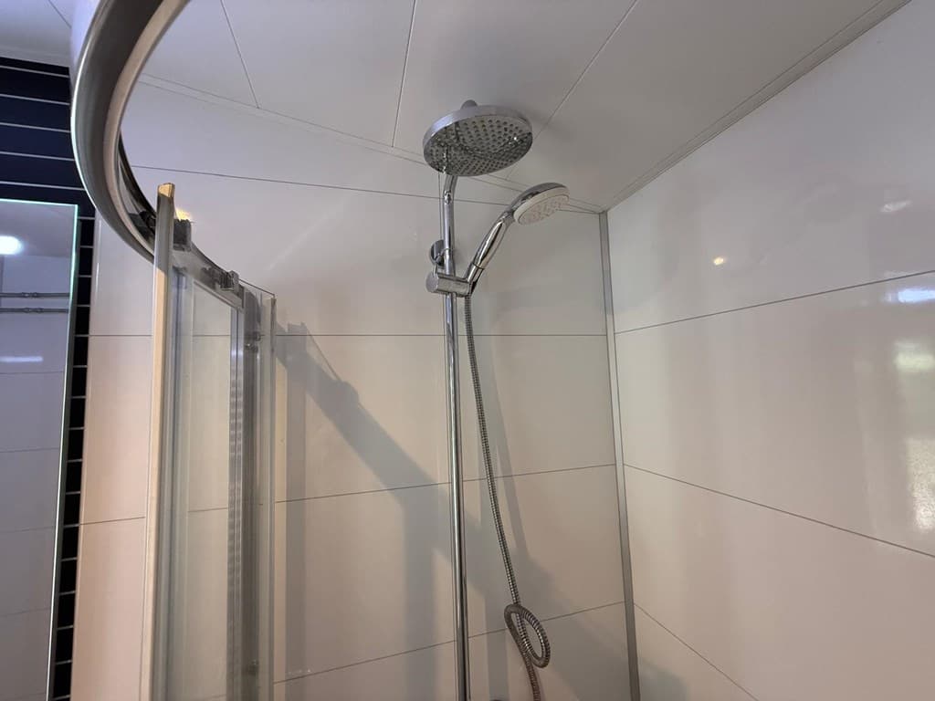 Moderne douchecabine met glazenschuifdeur en dubbele regendouchekop in een lichte badkamer.