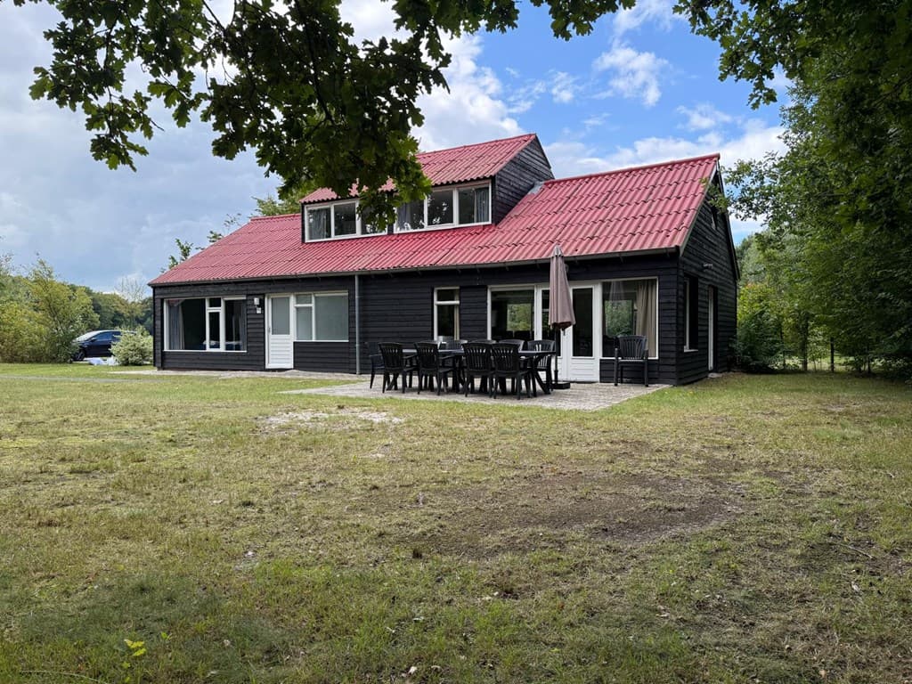 Zwarte vakantiewoning met rode dakbedekking, een omheinde tuin en een terras met tafels en stoelen