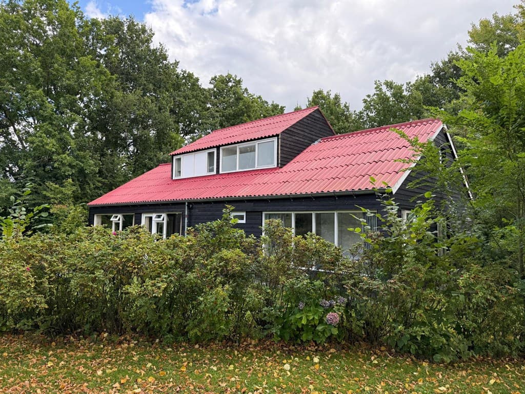 Zwarte vakantiewoning met een rood dak, omringd door onderhoudsarme groene begroeiing en bomen