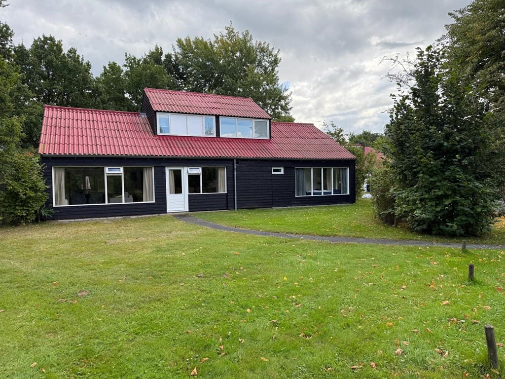 Zwart hout afgewerkt huis met rode dakpannen, grote ramen en een grasveld eromheen met bomen en struiken.