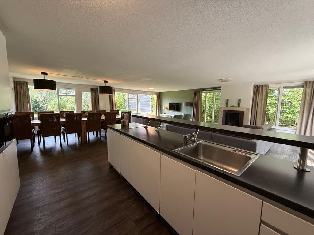 Ruime open keuken met eetkamer en woonkamer, veel natuurlijk licht en zicht op de groene omgeving.