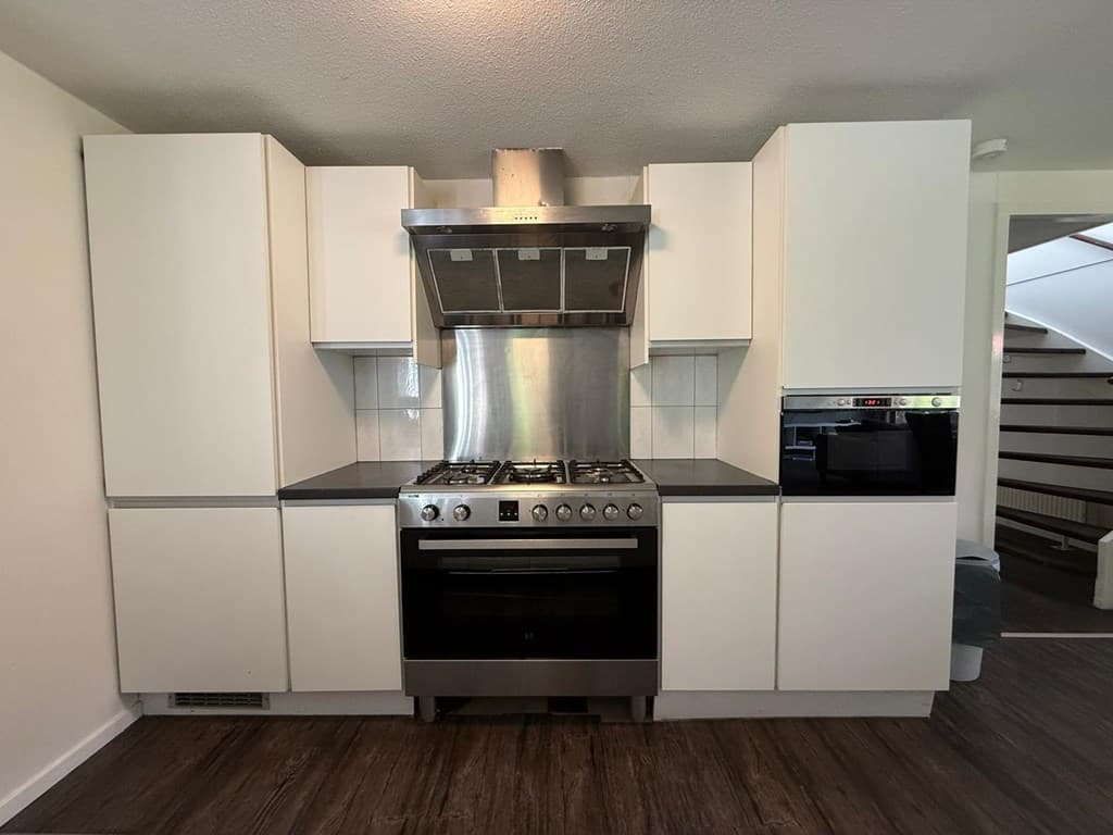 Moderne keuken met witte kastjes, RVS afzuigkap en een gasfornuis met oven.