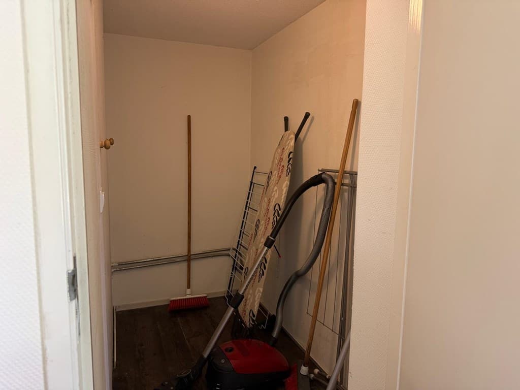 Opbergruimte met een stofzuiger, een bezem, een trapladder en een paar stokken tegen de muur.