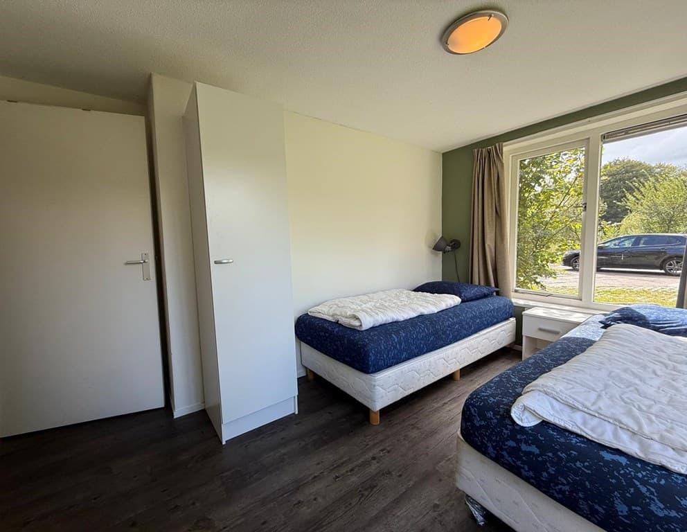 Slaapkamer met twee eenpersoonsbedden, kast en raam met uitzicht op buitenruimte.