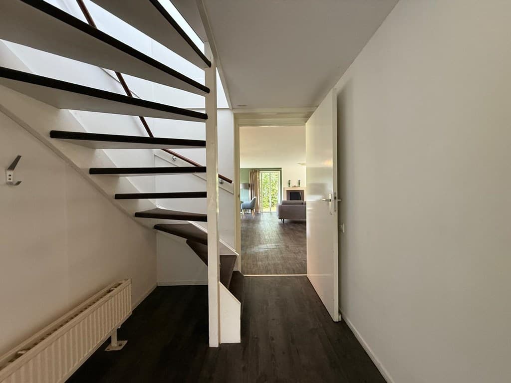 Entree met een trap naar boven en zicht op een lichte woonkamer met openslaande deuren naar buiten