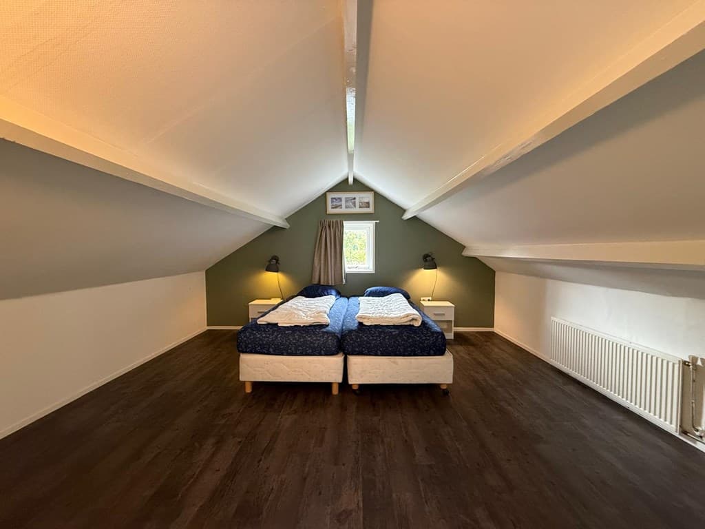 Sfeervolle zolderkamer met twee eenpersoonsbedden, houten vloer en schuin dak met meubels en raam.