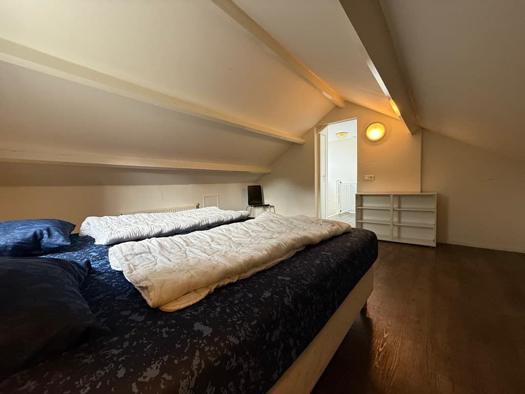 Slaapkamer met twee bedden, houten vloer en een kast tegen de muur onder het schuine dak.