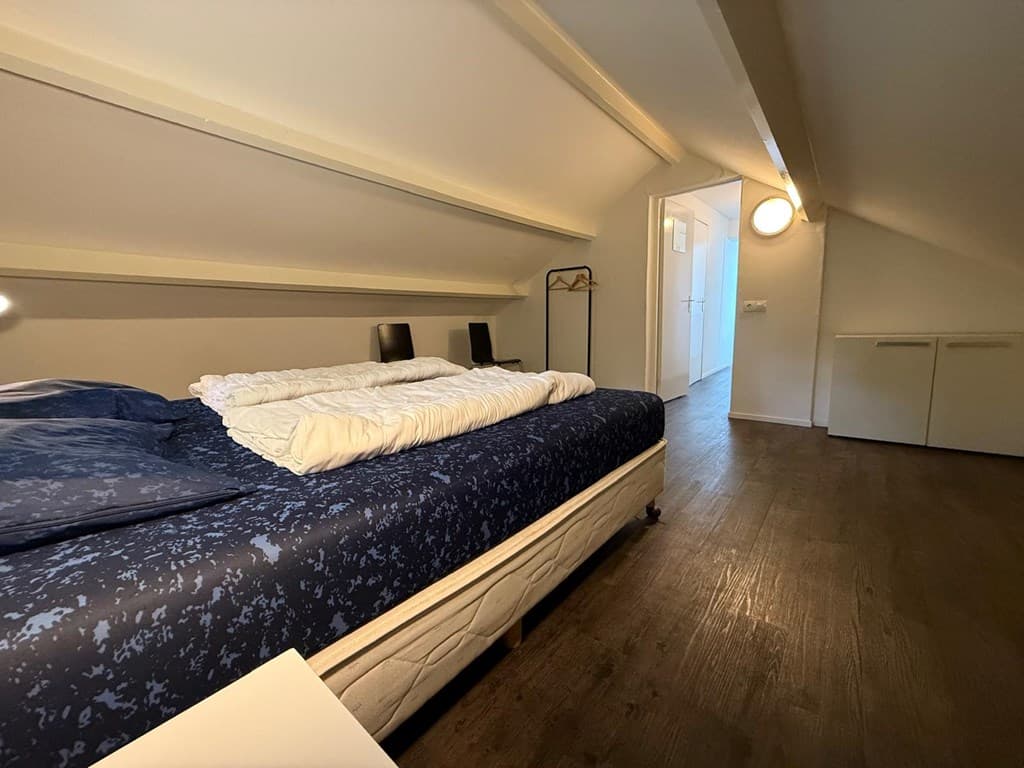 Ruime slaapkamer met een tweepersoonsbed, nachtkastjes en toegang tot een lichte gang.