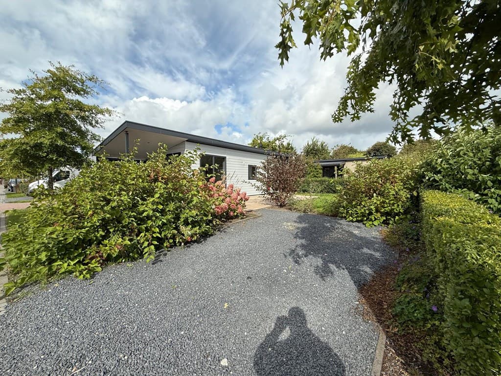 Buitenaanzicht van een vakantiewoning met een grindpad, groenstroken en struiken in EuroParcs Markermeer.
