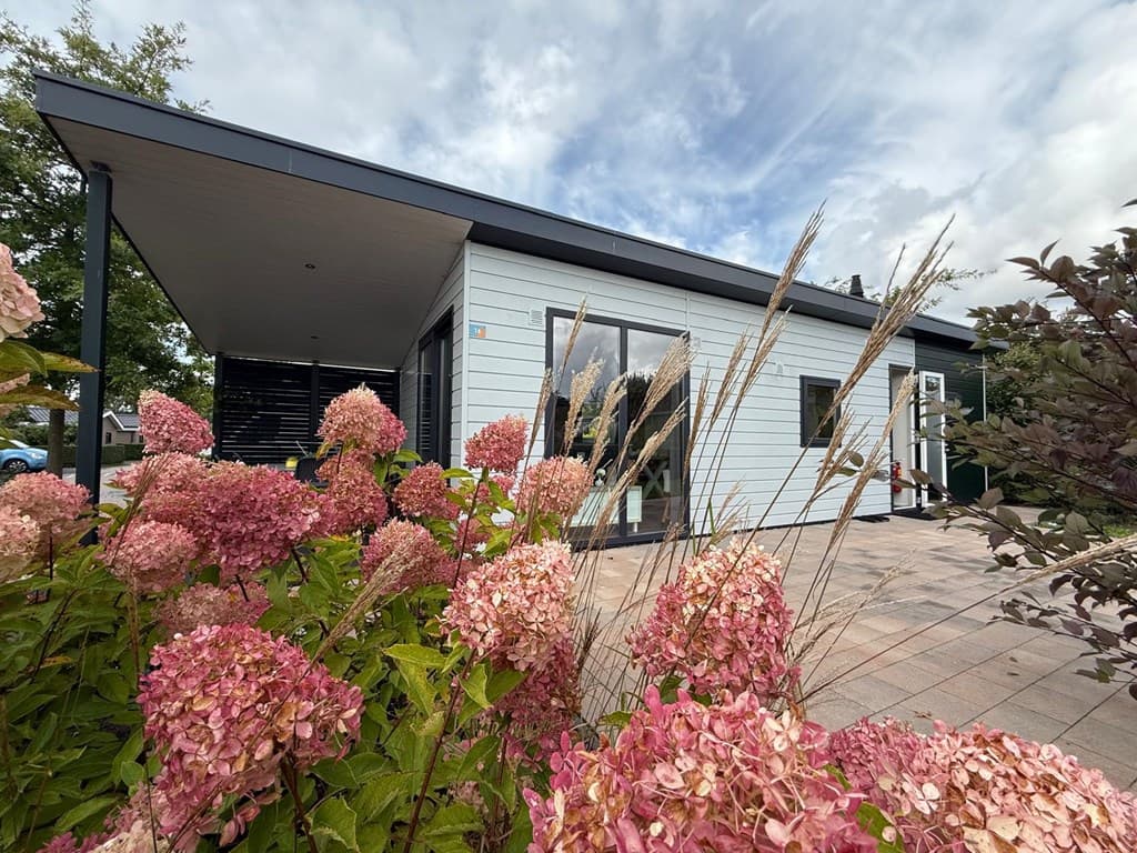 Moderne vakantiewoning omringd door bloeiende hortensia's en een betegeld terras met een heldere lucht op de achtergrond