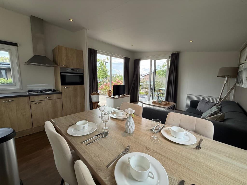 Eetkamertafel met servies en zithoek bij grote ramen met uitzicht op buitenruimte in moderne vakantiewoning