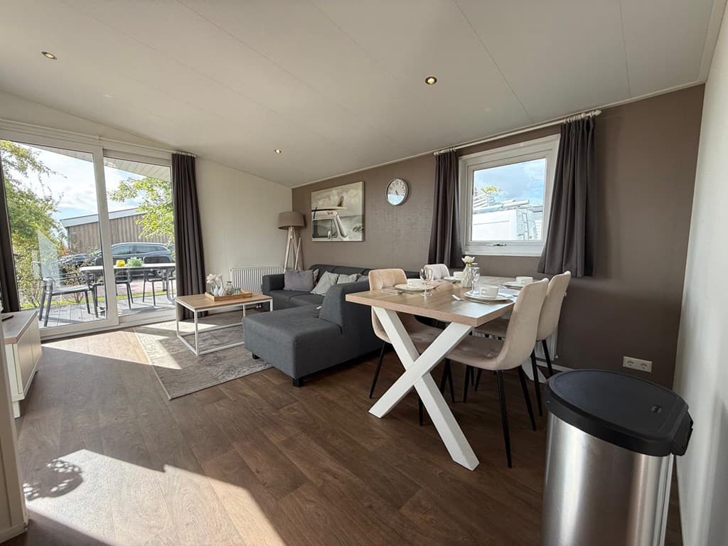 Onderdeel van een vakantiewoning met een zithoek, eettafel en grote ramen met uitzicht op het terras.