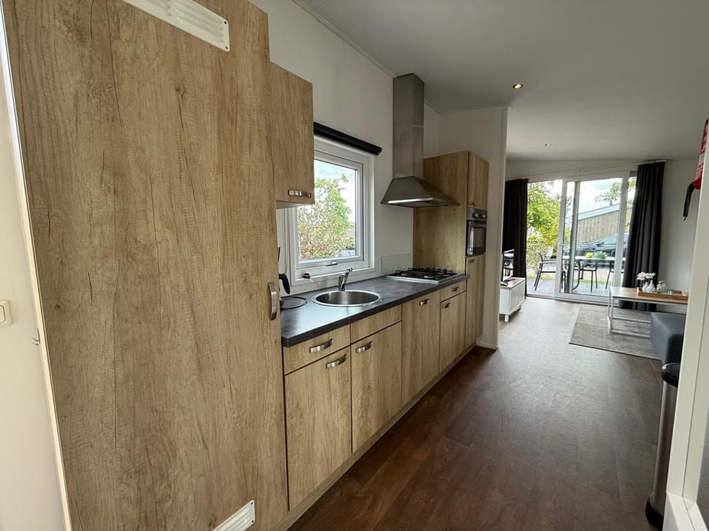 Keuken met houten kasten, spoelbak, kookplaat en oven, met toegang tot een zithoek en terras bij EuroParcs Markermeer