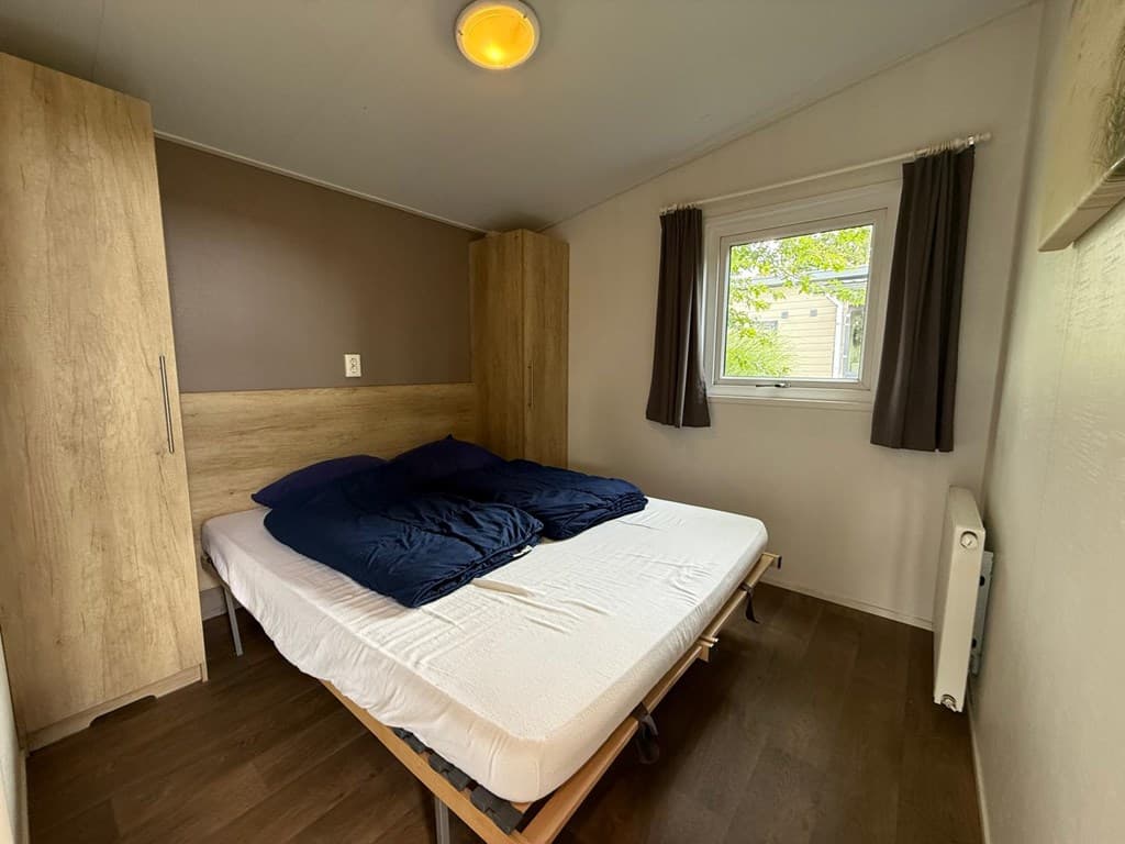 Slaapkamer met tweepersoonsbed en kast, raam met uitzicht op tuin, neutrale kleuren en houten vloer