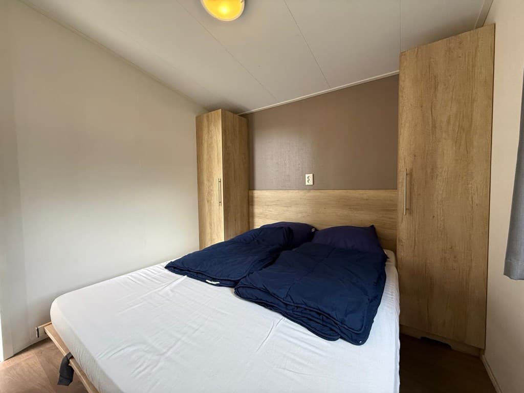 Slaapkamer met een tweepersoonsbed, houten kasten en lichtgrijze muren.