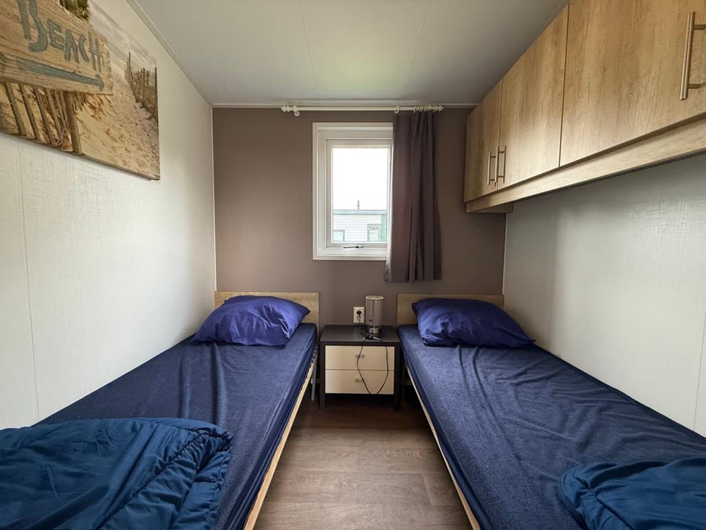 Slaapkamer met twee eenpersoonsbedden, nachtkastje en raam met uitzicht naar buiten.