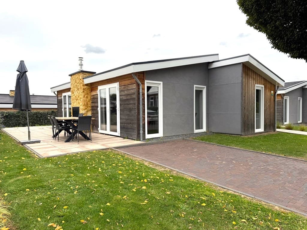 Modern vakantiehuis met houten gevel, terras en tuinmeubilair, gelegen in een groene omgeving met een stenen pad.
