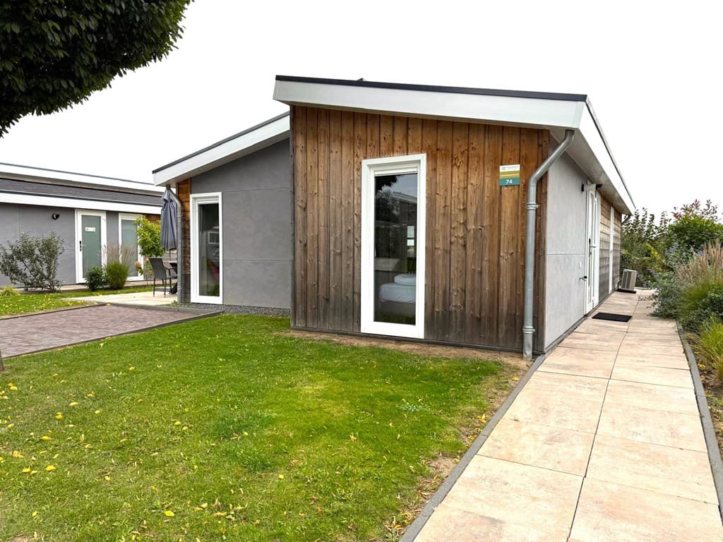 Moderne vakantiewoning met houten gevel, grote ramen en een omliggende groene tuin in Green Resort Mooi Bemelen.