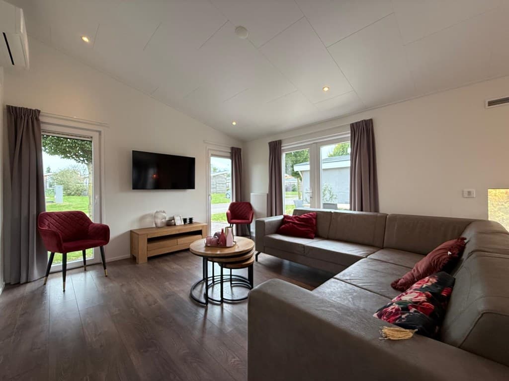Uitzicht op een moderne woonkamer met een L-vormige bank, stoelen, een salontafel en een tv aan de muur