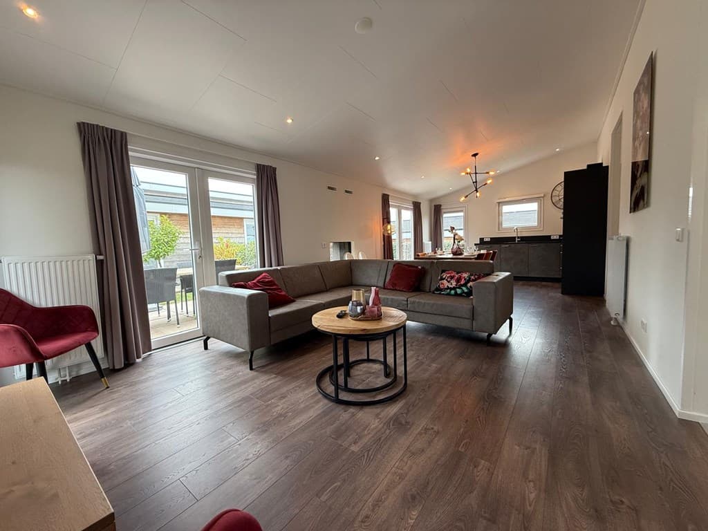 Ruime woonkamer met moderne inrichting, grote raampartij en toegang tot terras, zicht op keuken in achtergrond.