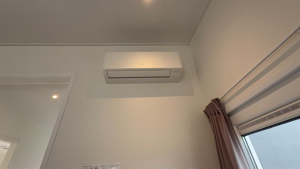 Wandairconditioner boven een raam met gordijnen in een lichte kamer