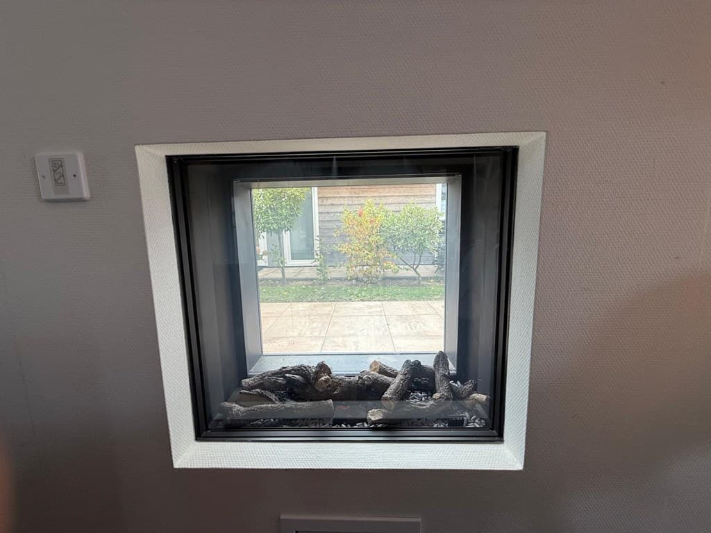 Gedeeltelijke zicht op een gashaard met een vierkant raam aan de muur met uitzicht op de buitenruimte.