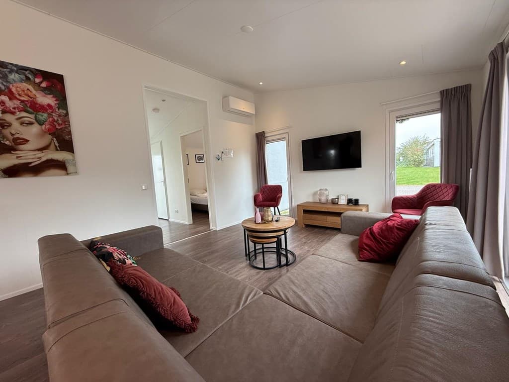 Ruime woonkamer met een bank, fauteuils, tv en kunst aan de muur in Green Resort Mooi Bemelen.