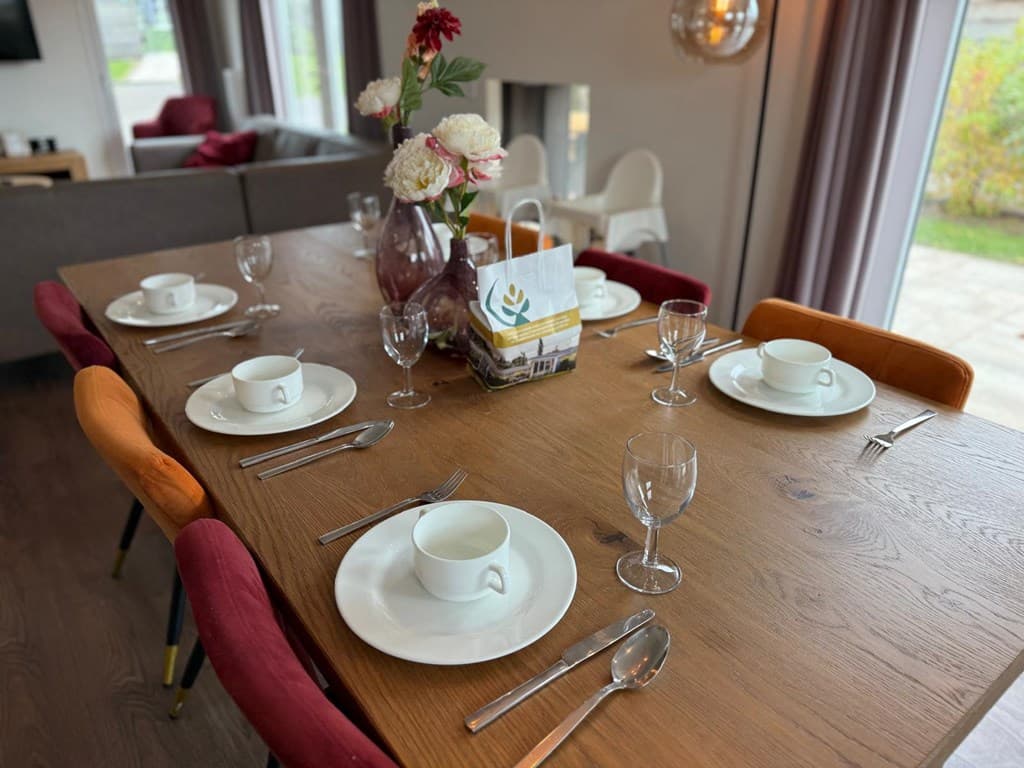 Eettafel met zes borden, glazen en bestek, een vaas met bloemen en een decoratieve mand.