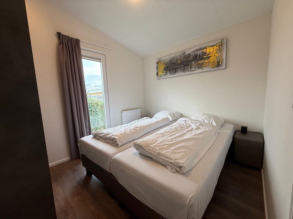 Slaapkamer met twee eenpersoonsbedden, raam met tuinzicht en lichte wanddecoratie.