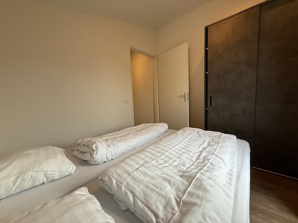 Slaapkamer met twee eenpersoonsbedden, een kast en een deur naar een andere ruimte.