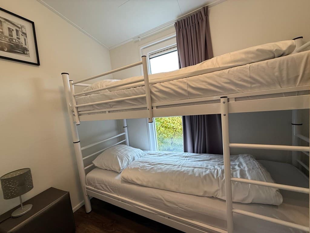 Slaapkamer met stapelbed en een eenpersoonsbed, raam met uitzicht op groen en gordijnen aan de zijkant.