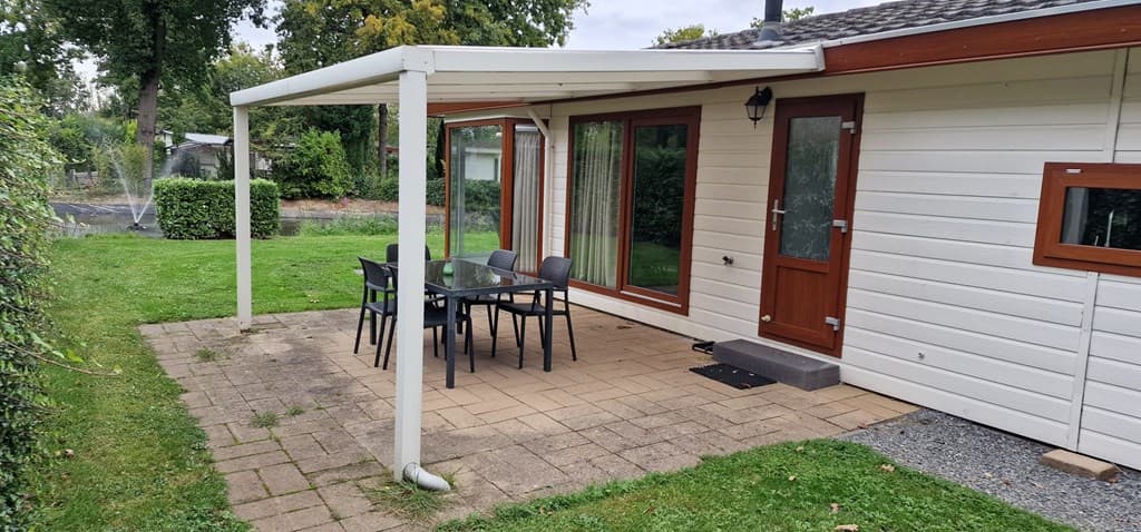 Tuin met terrasoverkapping en zithoek bestaande uit een glazen tafel met vier stoelen en uitzicht op groene grasvelden