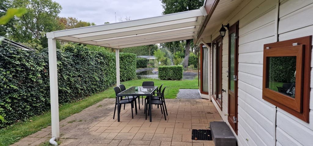 Overdekt terras met een eettafel en stoelen, omgeven door gras en groene hekwerk