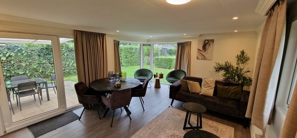 Moderne woonkamer met grote ramen, eetgedeelte, zithoek en toegang tot de tuin met groene afscheiding