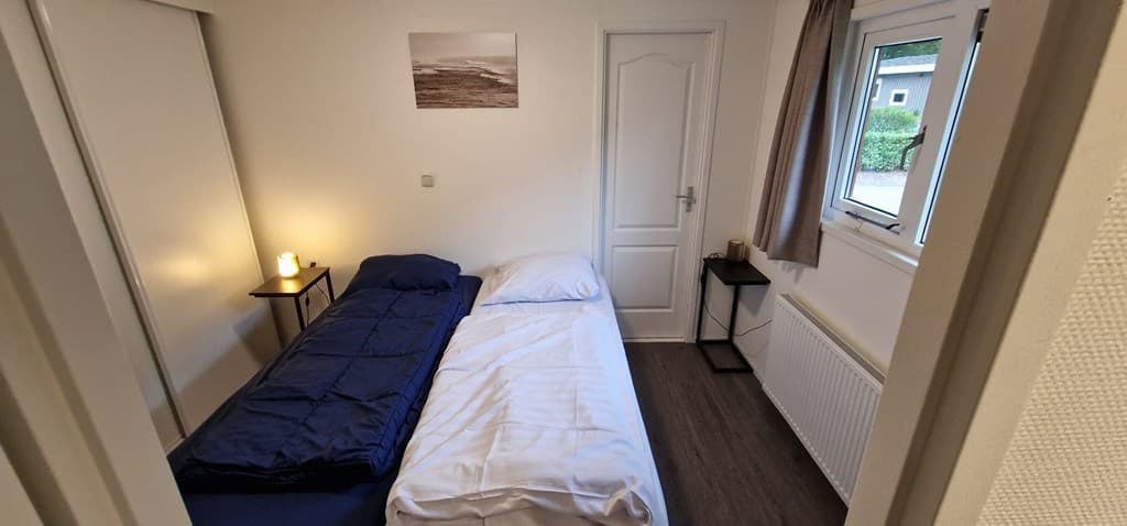 Slaapkamer met twee eenpersoonsbedden, nachtkastje en raam met uitzicht op de buitenruimte.