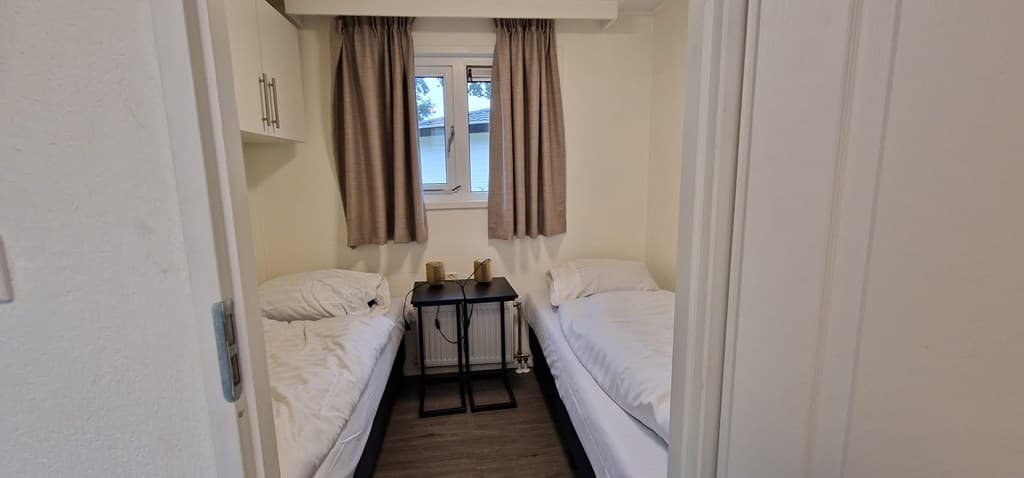 Slaapkamer met twee eenpersoonsbedden, raam met gordijnen en een klein bijzettafel tussen de bedden