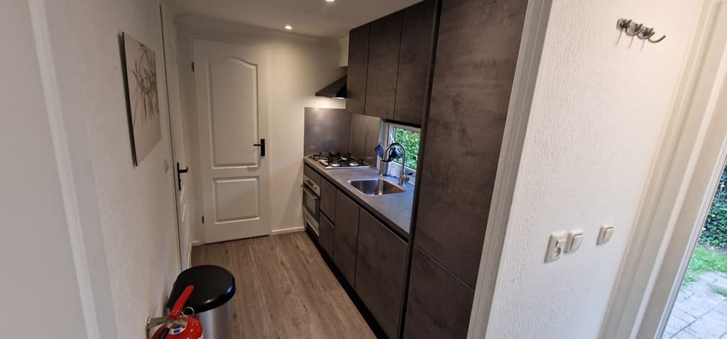 Moderne keuken met grijze kastjes, gasfornuis en spoelbak, uitzicht op buitenruimte en nette afwerking.