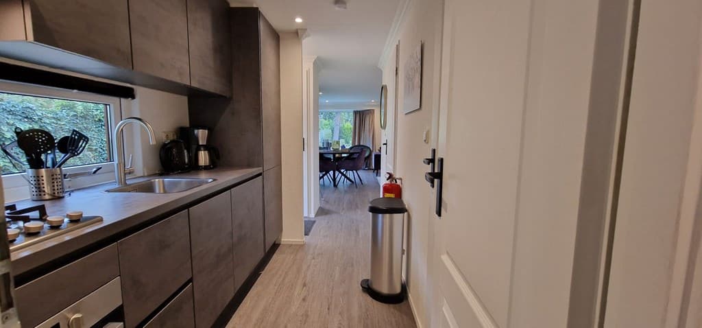 Moderne keuken met inbouwapparatuur en een gang naar een eet- en woongedeelte met grote ramen en een tafel.