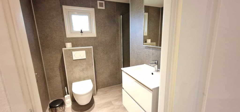 Moderne badkamer met een ligbad, wastafel met spiegel en toilet, afgewerkt met stenen muren en grijze vloer.