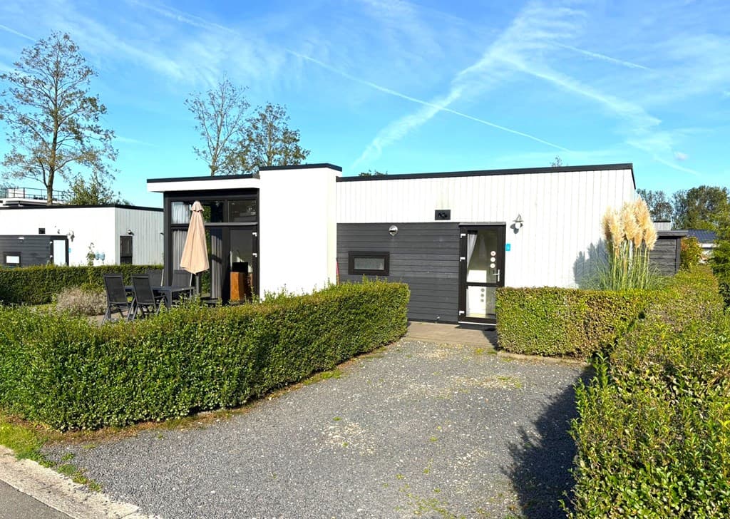 Moderne vakantiewoning met een groene tuin en terras, gelegen in een rustige omgeving met blauwe lucht en bomen.