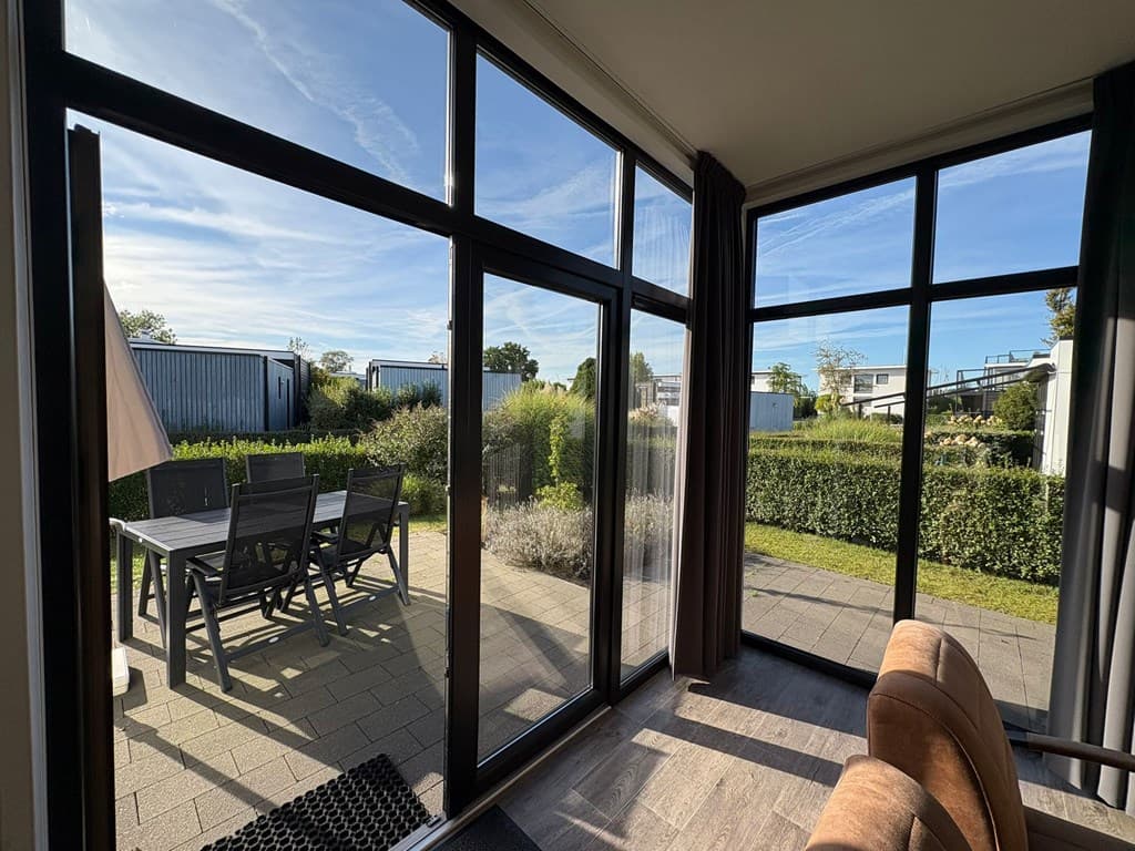 Zicht op tuin met terras en tuinmeubilair, omringd door groene hagen en een helderblauwe lucht.