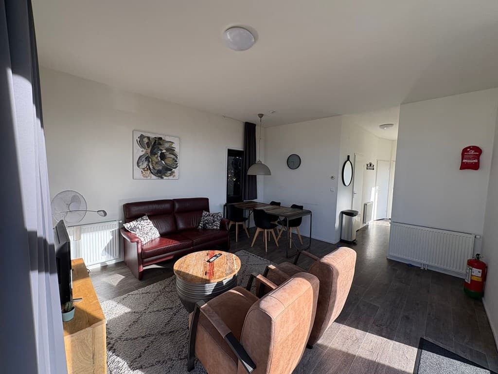 Ruime woonkamer met een zithoek, dining tafel en toegang tot de keuken in lichte kleuren en moderne inrichting